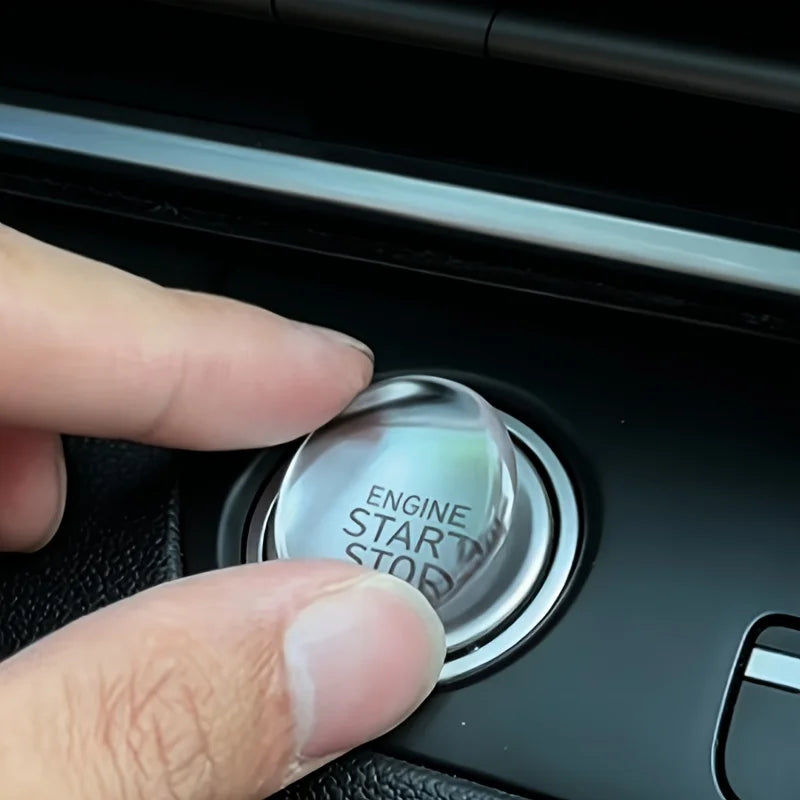 A hand presses a crystal clear car ignition button protector labeled Engine Start Stop on a dark surface.