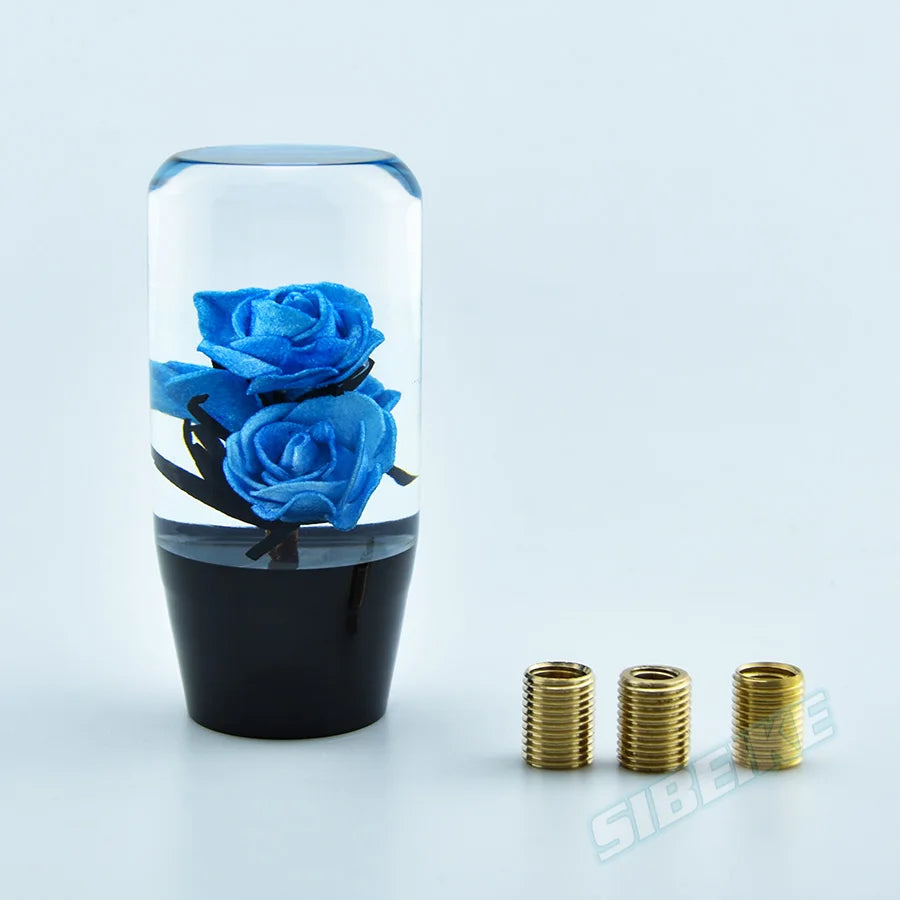 A clear glass cylinder containing a blue crystal flower gear shift knob and adapters.