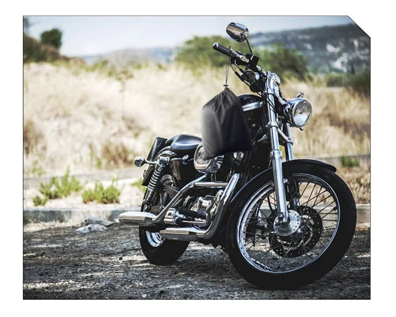 Una motocicleta negra estacionada en un camino de tierra con una cubierta impermeable negra sobre el asiento.