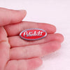 A hand holds a red and silver oval Peterbilt truck emblem pin brooch.