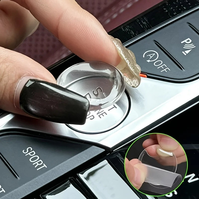 A hand is pressing a crystal clear car ignition button protector onto a vehicle's ignition switch.
