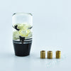 A clear glass cylinder containing a white rose flower and black gear shift knob adapters.