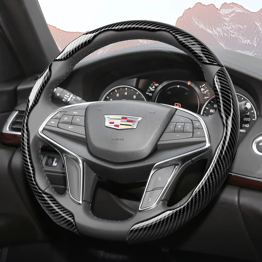 A close-up view of a black steering wheel with a sporty carbon fiber patterned cover inside a car interior.