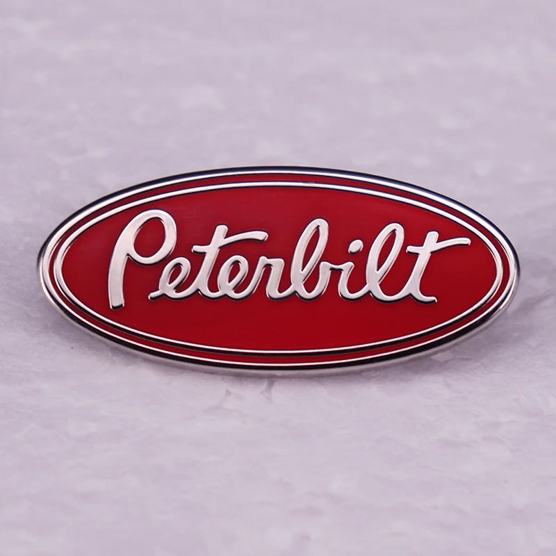 A red oval metal pin featuring the white Peterbilt truck logo on a silver rim.