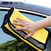 A hand is wiping a dark car surface with a yellow microfiber car wash towel.