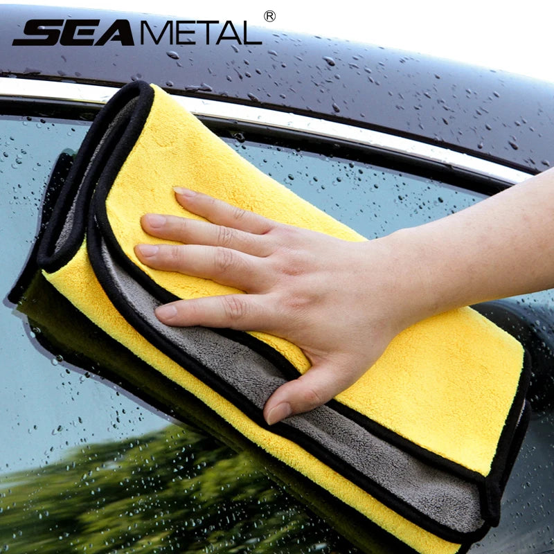 A hand is wiping a dark car surface with a yellow microfiber car wash towel.