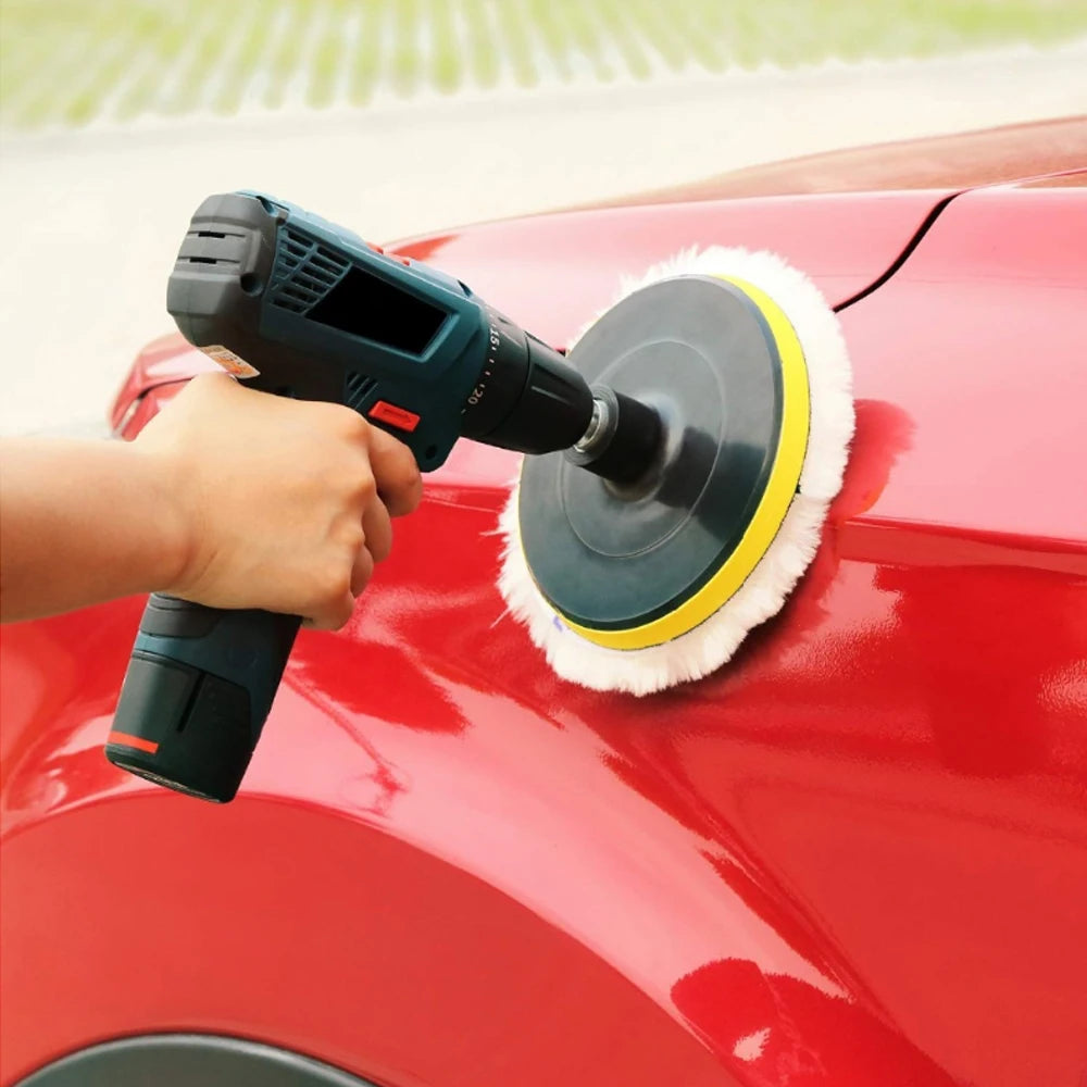 A hand uses a black electric polisher with a white wool buffing pad on a red car surface.