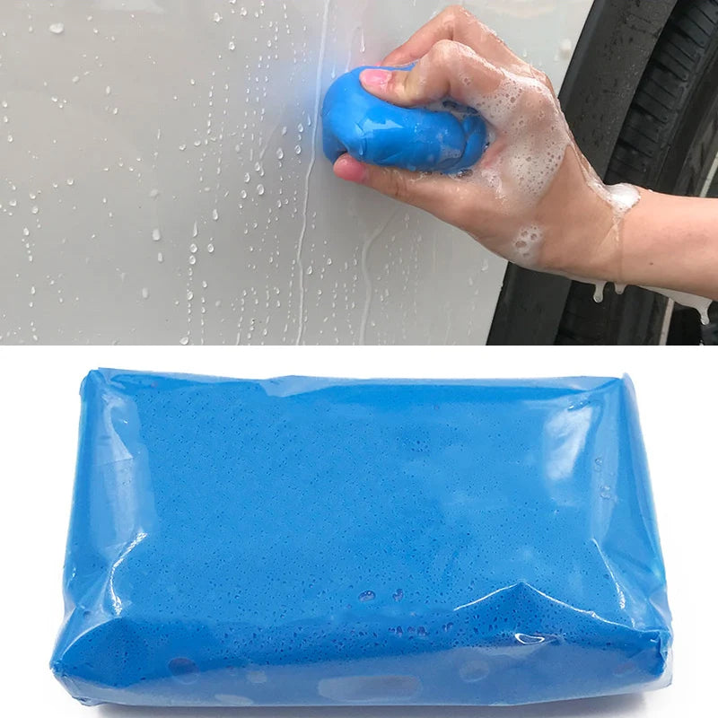 A hand applies blue magic clay bar to a car surface, with a blue plastic bar visible in the foreground.