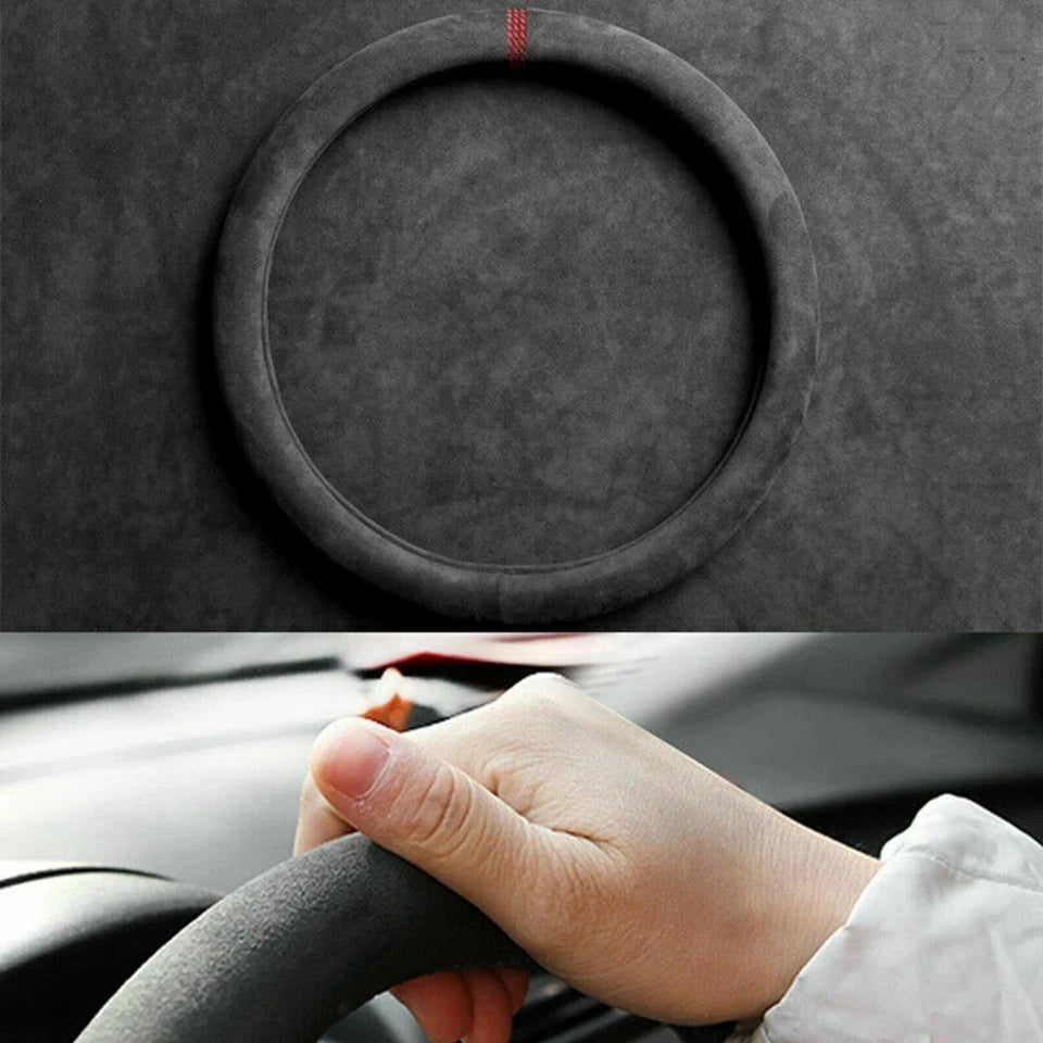 A hand grips a dark suede steering wheel cover on a car's steering wheel.