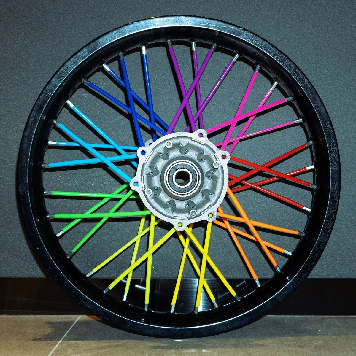 A black motorcycle wheel rim with numerous colored spokes, including blue, green, yellow, and red.
