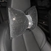 Primer plano de un cojín para el cuello de coche de pedrería cristalina con diseño de lazo sobre un asiento de cuero oscuro.