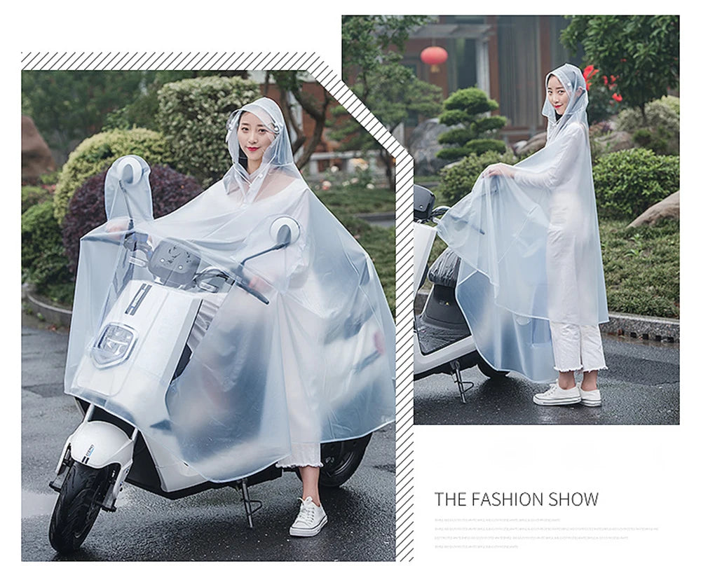 A woman wearing a transparent windproof motorcycle rain poncho is riding a motorcycle outdoors.