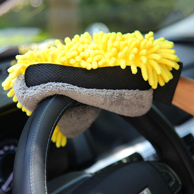 Yellow microfiber chenille car wash mitt resting on a black steering wheel.
