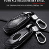 A black carbon fiber key shell with a silver key fob is displayed on a dark leather surface.