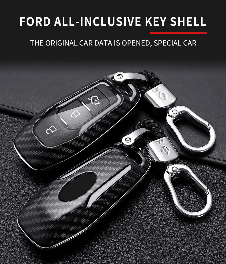 A black carbon fiber key shell with a silver key fob is displayed on a dark leather surface.