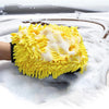 A yellow microfiber chenille car wash mitt with white fibers is shown resting on a wet, icy surface.