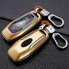 A gold-colored car key cover with a silver keyring and leather strap resting on a black surface.