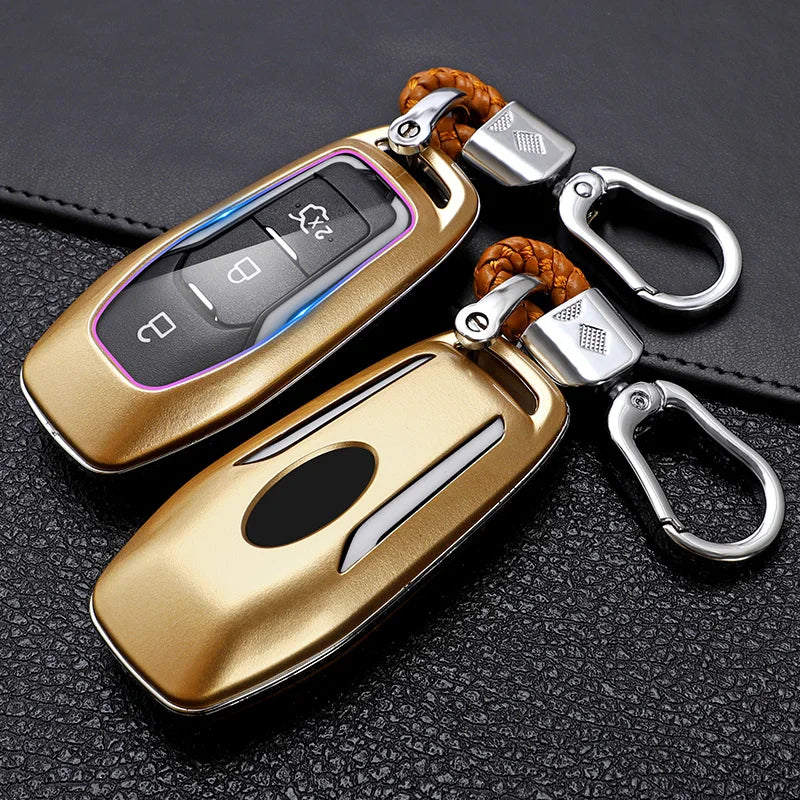 A gold-colored car key cover with a silver keyring and leather strap resting on a black surface.