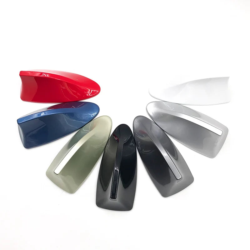 A collection of various colored and silver car shark fin antenna covers displayed against a white background.