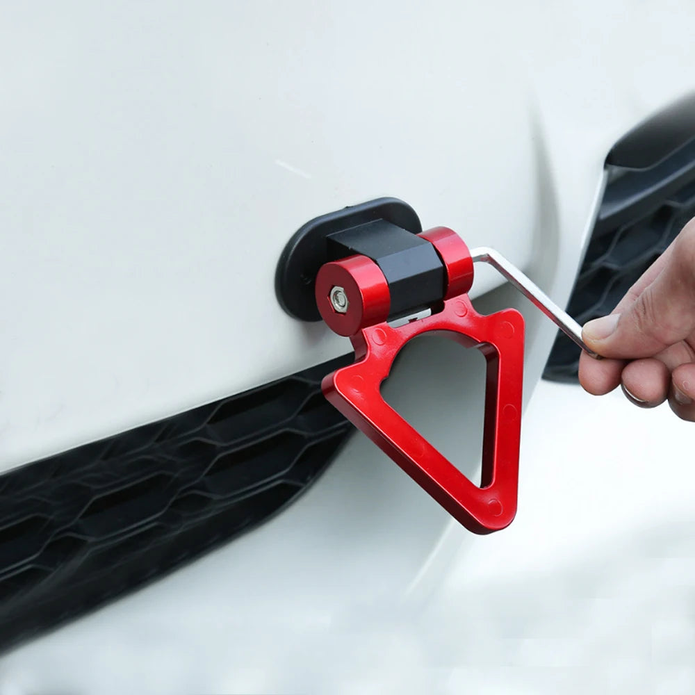 A hand is installing a red and black racing style car tow hook onto a white vehicle's body panel.