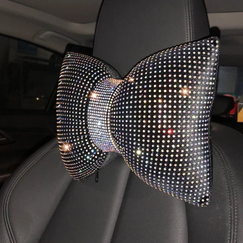 Un cojín de cuello de coche de cristal de pedrería negra está apoyado en un asiento de cuero oscuro.
