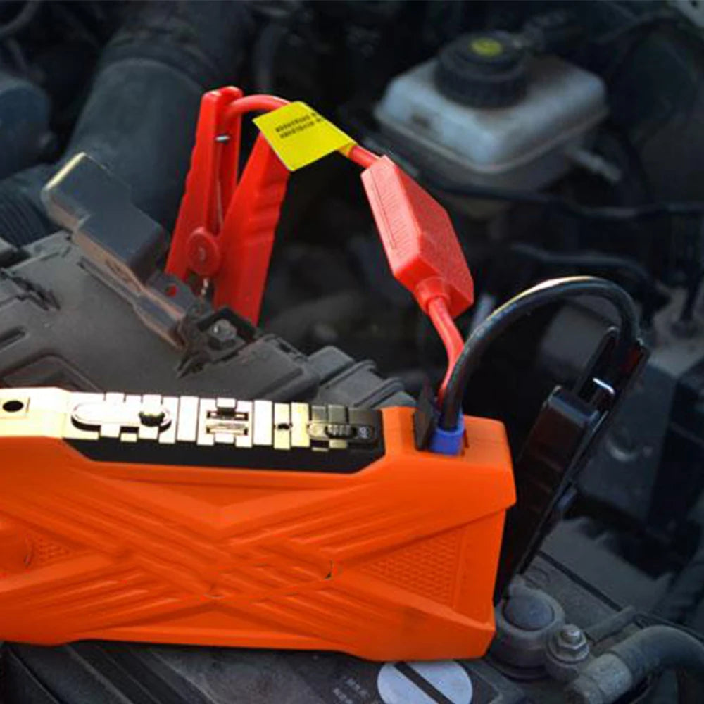 An orange battery jump starter cable is connected to a vehicle's battery terminal.