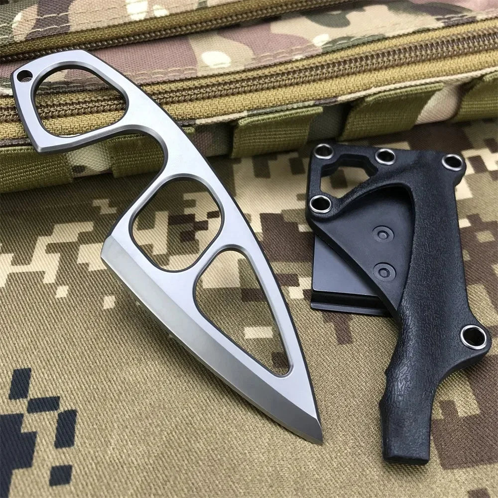 A silver fixed blade knife is shown next to a black handle, resting on a camouflage fabric background.