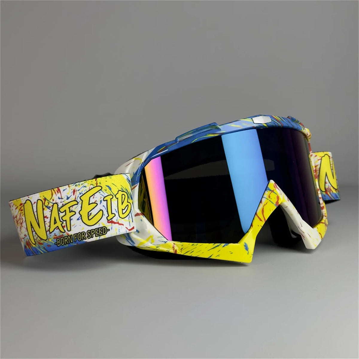 Un par de gafas de motocicleta amarillas y blancas con lente colorido sobre una superficie gris.