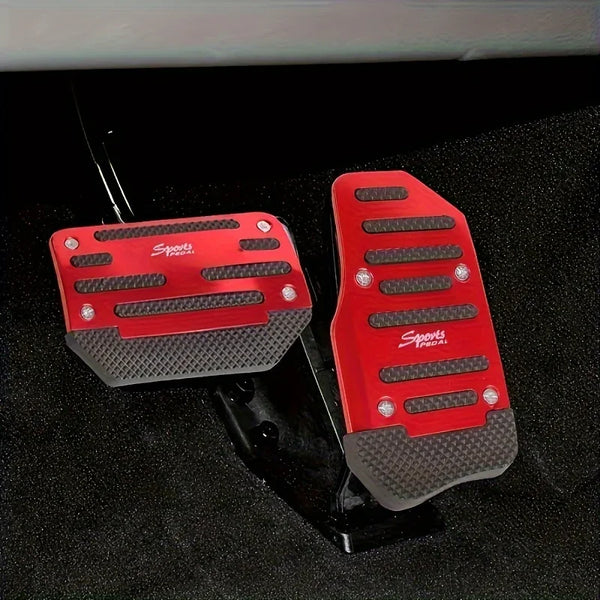 A pair of red and gray aluminum foot pedals for a manual car, displayed on a black surface.