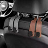 Car headrest hooks in brown leather attach to a black car seat for bag organization.