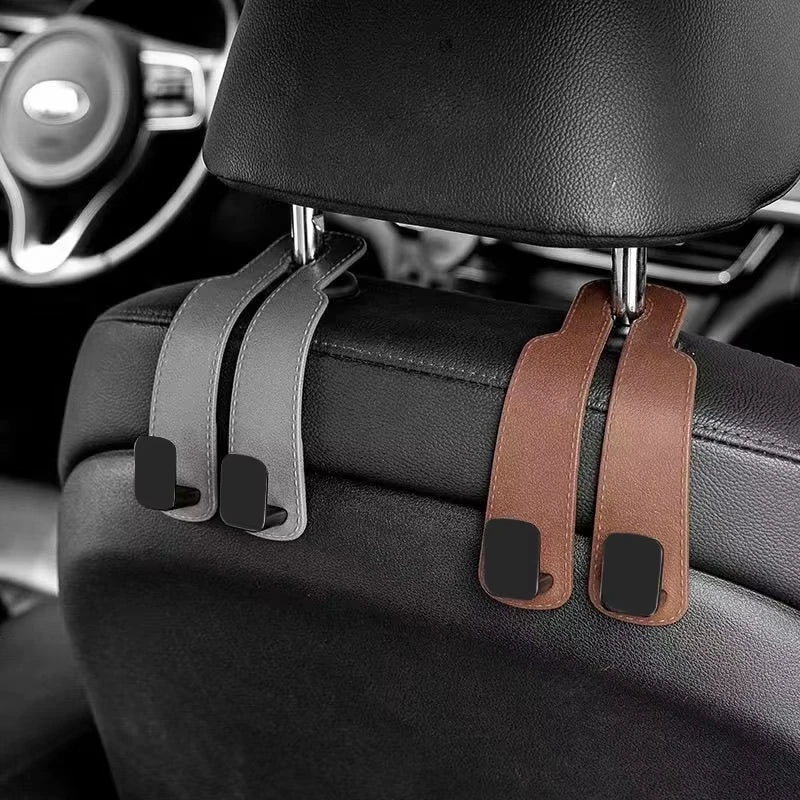 Car headrest hooks in brown leather attach to a black car seat for bag organization.