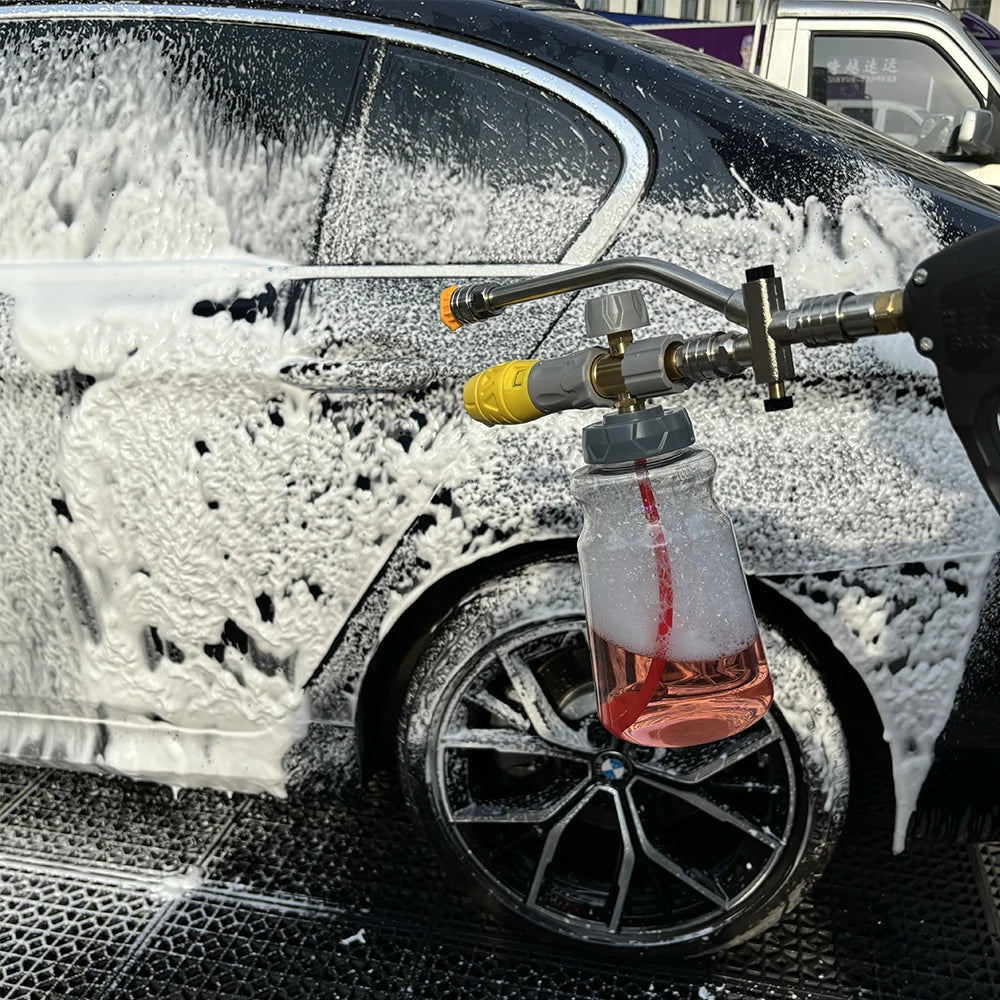A close-up of a black car being cleaned with white foam from a pressure washer adapter.