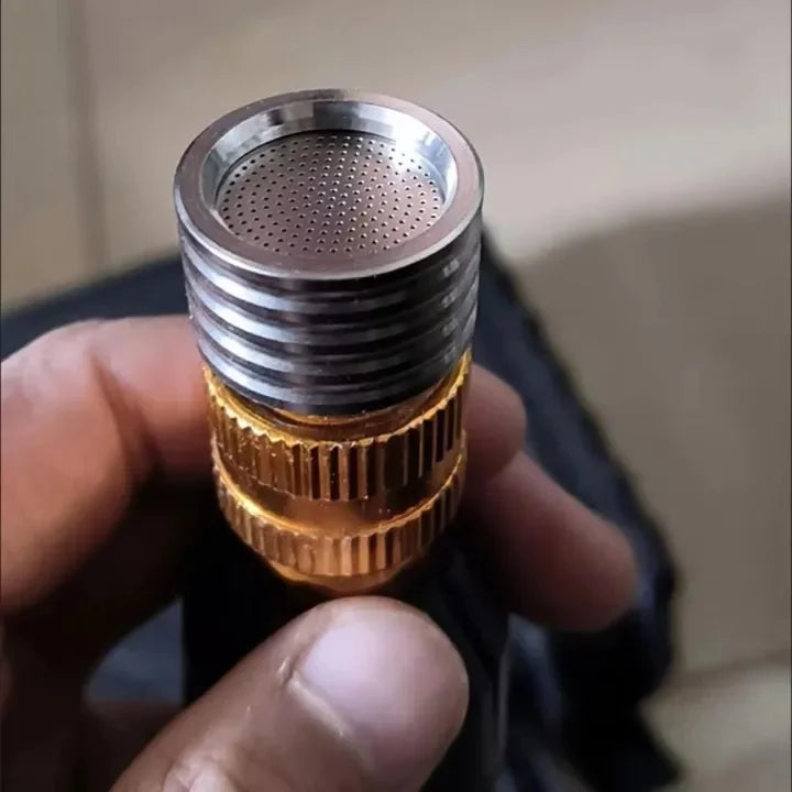 A hand holds a high-pressure stainless steel shower head nozzle with a brass collar and perforated metal tip.