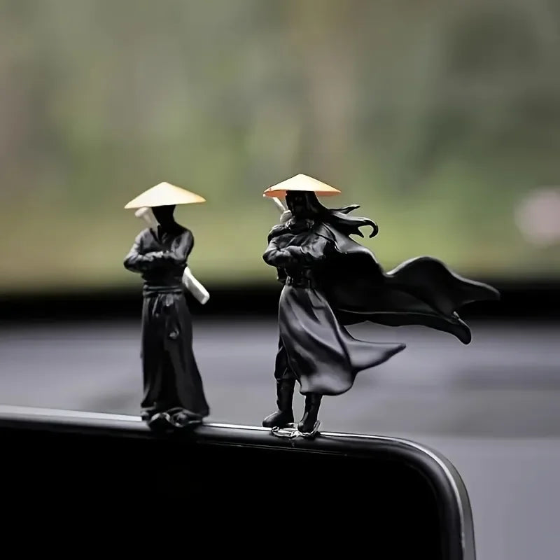 A pair of black mini samurai statues with traditional hats are displayed on a dark surface.