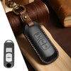 A black leather car key fob cover with a brass keyring is shown resting on a wooden surface.