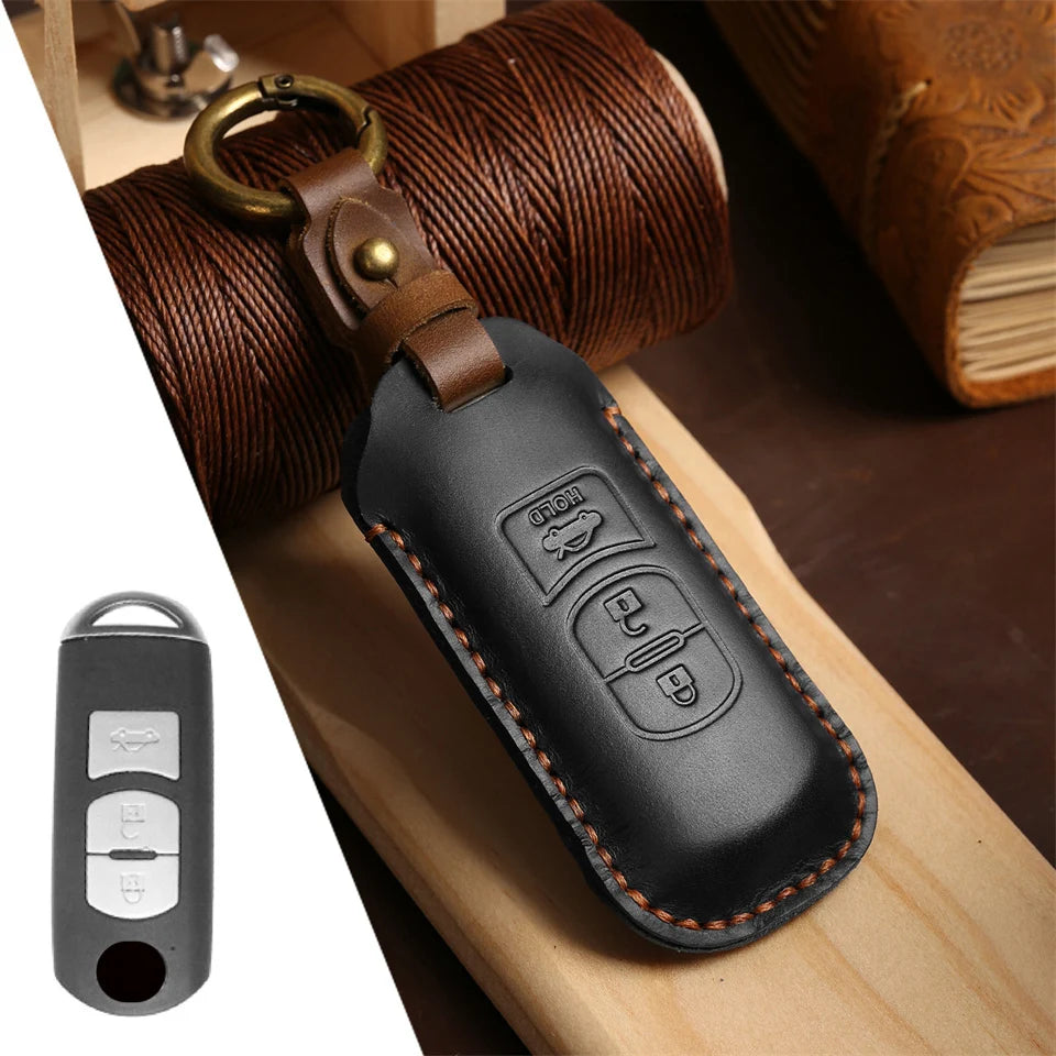 A black leather car key fob cover with a brass keyring is shown resting on a wooden surface.