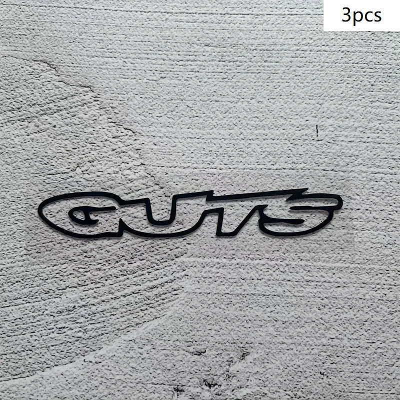 Three black vinyl decals spelling the word GUTS on a gray textured surface.
