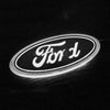 A close-up, black and white photo of a round Ford logo emblem with a bright white glow.