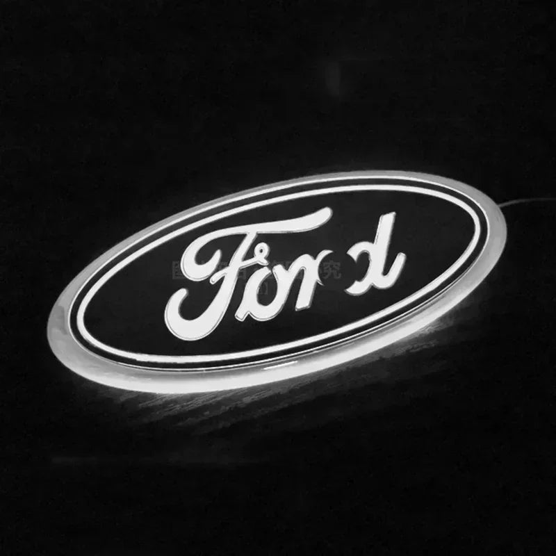 A close-up, black and white photo of a round Ford logo emblem with a bright white glow.