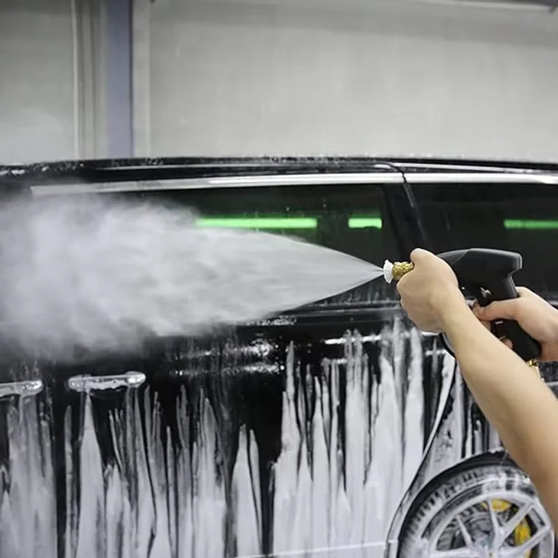 A hand is using a high-pressure cleaning gun to spray water onto the black and white paint of a vehicle.