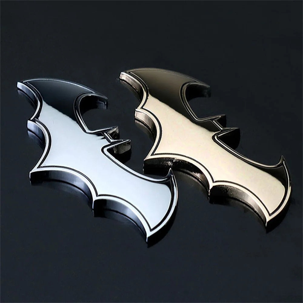 Zwei 3D-Metall-Bat-Aufkleber oder Abzeichen, eines silber und eines gold, vor dunklem Hintergrund dargestellt.