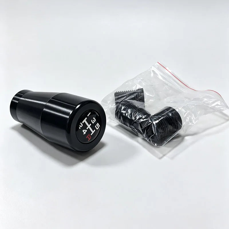 A black gear shift knob and a bag containing several black gear shift knobs.