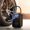Inflador eléctrico portátil negro con botón naranja junto a una rueda de coche.