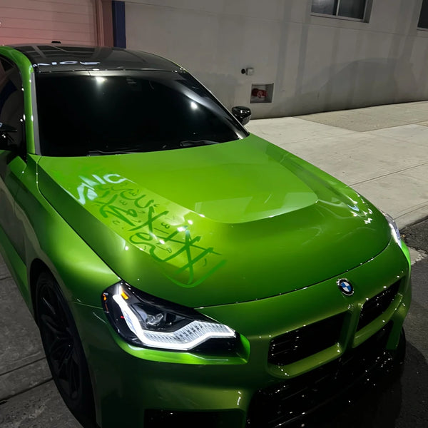A bright green BMW sports car with custom graffiti stickers on the hood parked outdoors.