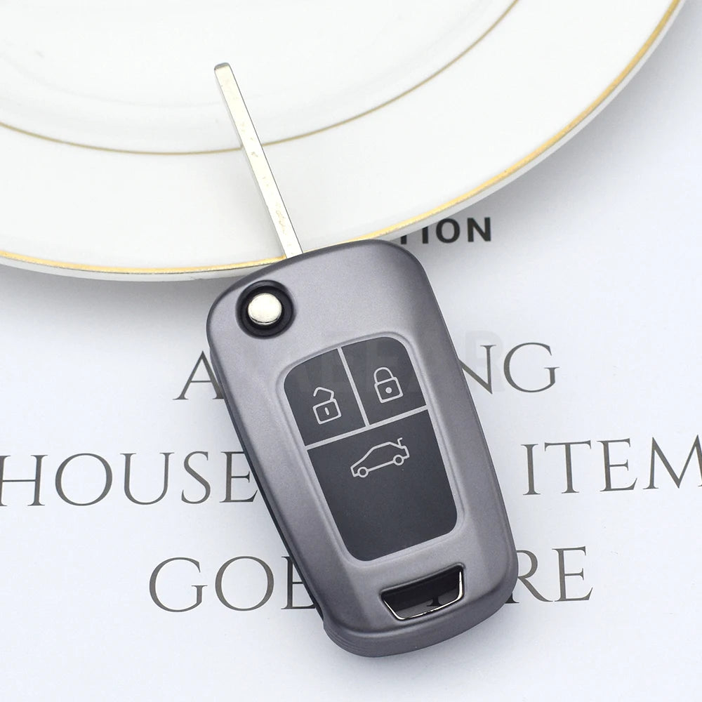 A close-up view of a dark gray universal car key cover with a metal key blade and a keyring, resting on a white surface.