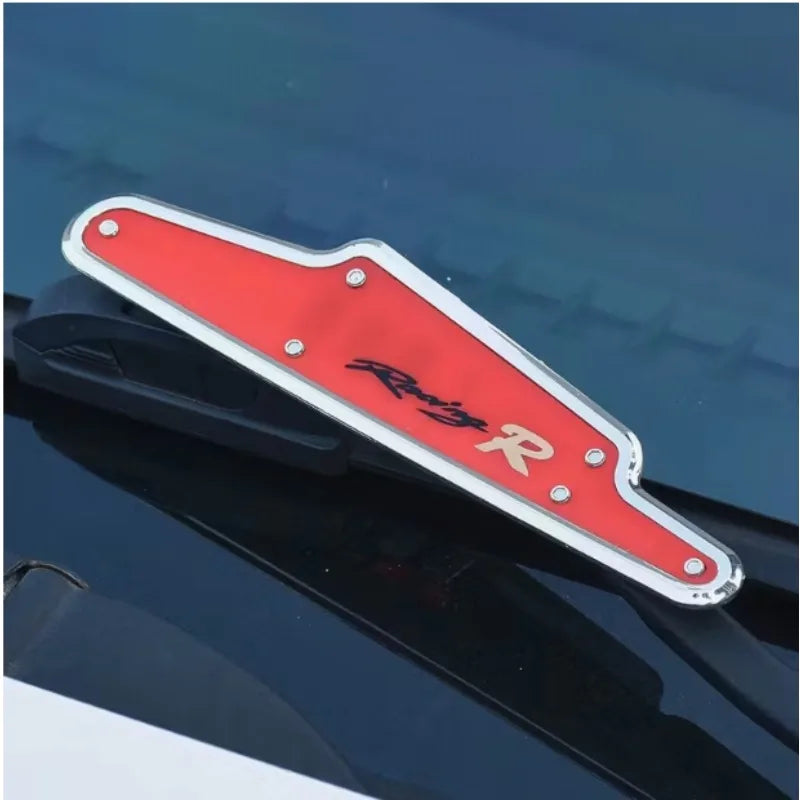 A red and silver car wiper pressure regulator booster is shown resting on a dark car surface.