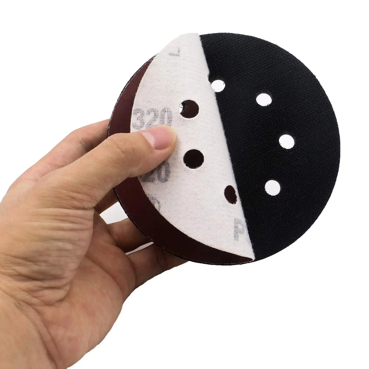 A hand holds a black abrasive interface pad with white markings and circular holes.