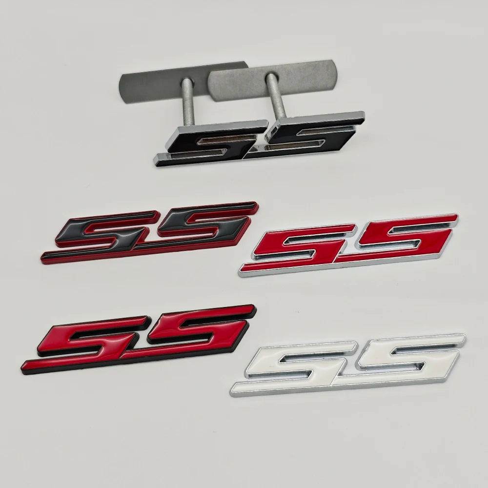 A collection of three metal SS/RS emblem badges in silver, red, and black finishes.