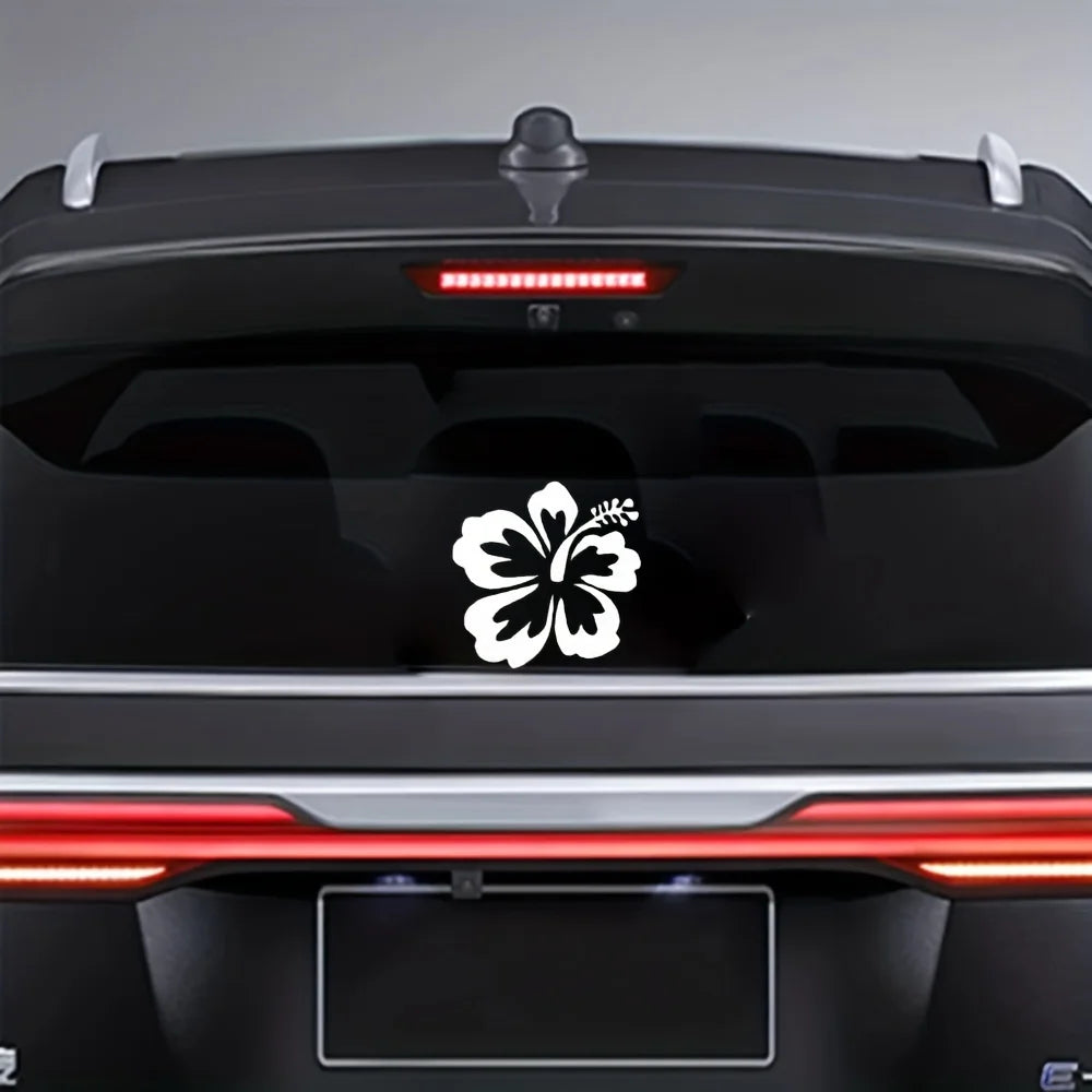 Nahaufnahme der Rückseite eines schwarzen Autos mit weißem Hibiskusblütenaufkleber und roten Rücklichtern.