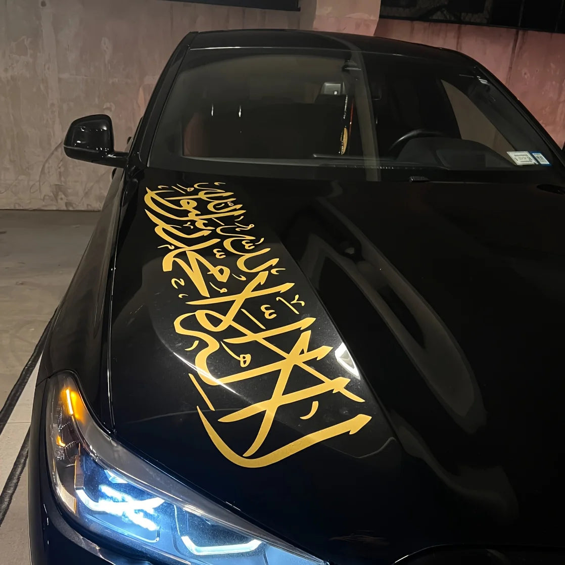 Une voiture noire ornée d'autocollants de calligraphie arabe dorée sur le capot et les phares.